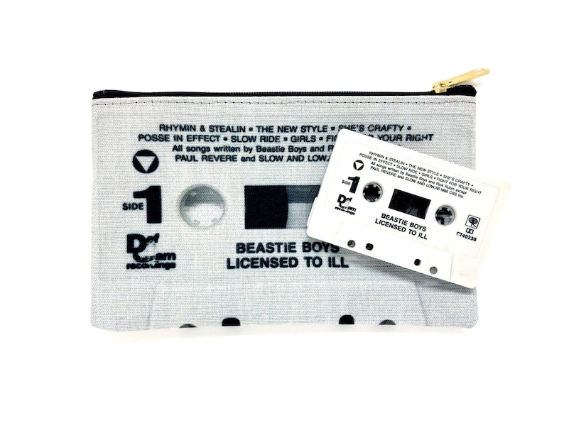 May include: A light gray cassette tape-themed zippered pouch with a gold zipper and a white cassette tape. The pouch features song titles and the text "BEASTIE BOYS LICENSED TO ILL". The cassette tape also has the same text.