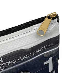 May include: A white and black zippered pouch with a gold-colored zipper pull. The pouch features the text "LAST DANCE" and the number "1". The zipper pull is marked with "YKK".