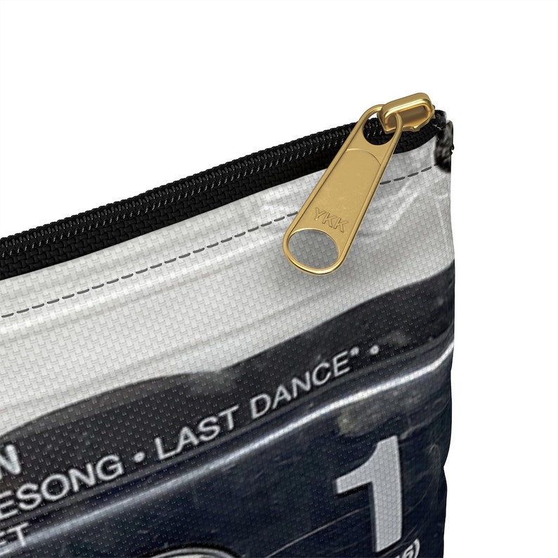 May include: A white and black zippered pouch with a gold-colored zipper pull. The pouch features the text "LAST DANCE" and the number "1". The zipper pull is marked with "YKK".