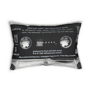 May include: A decorative pillow featuring a black cassette tape design with the text "nine inch nails the downward spiral." The pillow has a clear plastic border and includes song titles and production credits. The pillow is rectangular.