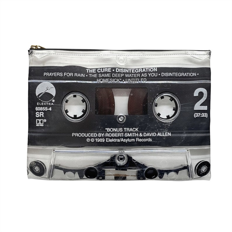May include: A clear, rectangular zipper pouch featuring a black and white cassette tape design. The tape design includes the text "THE CURE DISINTEGRATION" and other song titles. The pouch has a gold zipper and is on a white background.