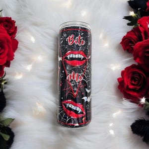 May include: A black and red stainless steel tumbler with a spiderweb design and the words "Bite Me" in white letters. The tumbler features a red and white vampire mouth with fangs.