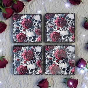May include: Four square stone coasters featuring a repeating pattern of human skulls, deep red roses, and small red hearts. The coasters have a rough, natural edge and a glossy surface finish, displaying a detailed gothic-inspired floral design.