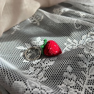 May include: A red and green crocheted strawberry keychain with a silver ring.