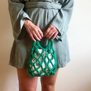 May include: A woman wearing a sage green wrap dress with long sleeves and a green crocheted mesh bag.