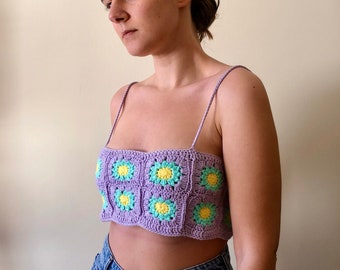 May include: A purple crochet top with a floral pattern. The top has a square neckline and thin straps. The flowers are yellow and green.