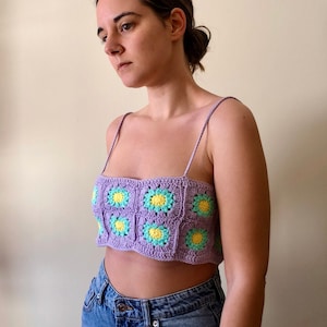 以下が含まれることがあります： 花柄の紫色のクロシェトップ。トップはスクエアネックで、細いストラップが付いています。花は黄色と緑色です。