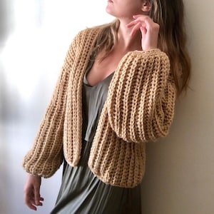 May include: A tan crocheted cardigan with long sleeves and a relaxed fit. The cardigan is open in the front and has a slightly cropped length.