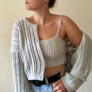 K&ouml;nnte beinhalten: Ein hellgraues H&auml;kel-Crop-Top und Cardigan-Set. Das Top ist ein &auml;rmelloses Tanktop und der Cardigan hat eine lockere Passform mit langen &Auml;rmeln.