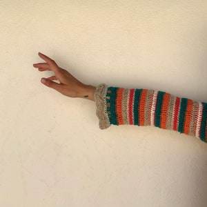 May include: A close-up of a striped crochet sleeve in orange, green, beige, and pink. The sleeve is partially rolled up, revealing a beige crocheted cuff.
