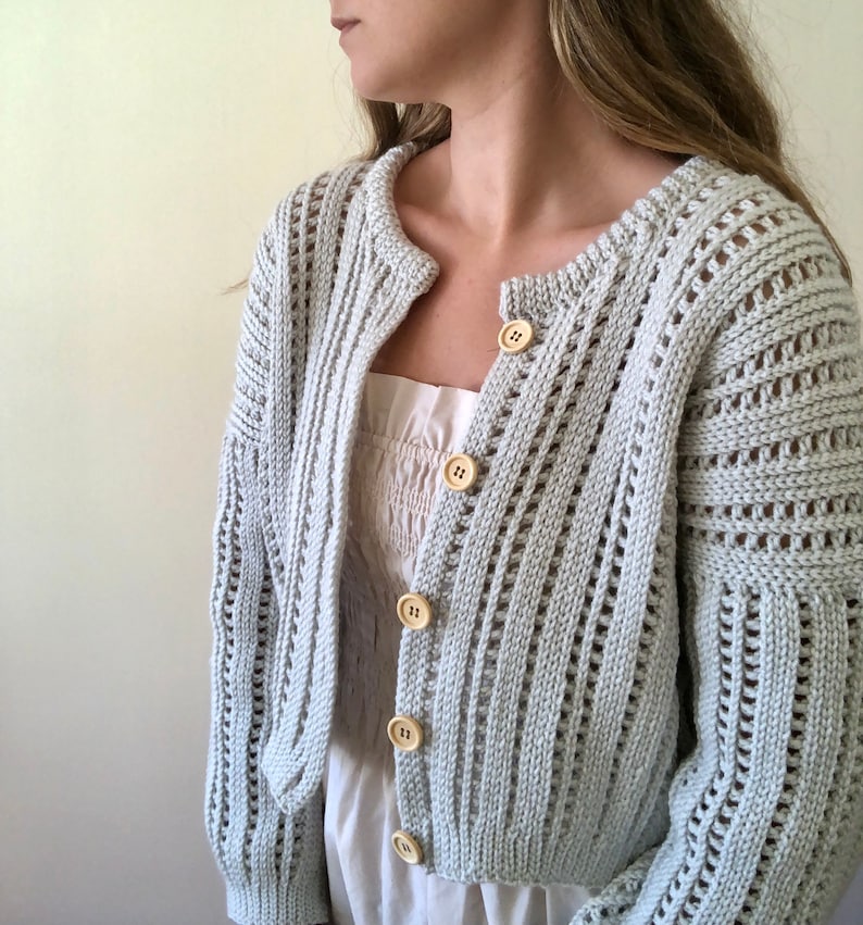 K&ouml;nnte beinhalten: Ein hellgrauer Strickcardigan mit Knopfleiste und leicht verk&uuml;rzter L&auml;nge. Der Cardigan hat ein zartes Lochmuster und ist aus weichem, leichtem Garn gefertigt.