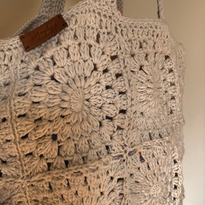 May include: A beige crocheted tote bag with a brown leather tag that says "The Bag Lady". The bag has a circular pattern.