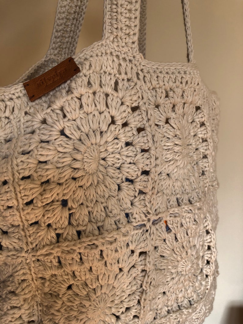 May include: A beige crocheted tote bag with a brown leather tag that says "The Bag Lady". The bag has a circular pattern.