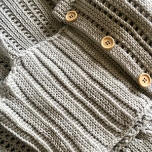 K&ouml;nnte beinhalten: Nahaufnahme eines grauen Strickjackens mit Holzkn&ouml;pfen. Der Cardigan hat ein strukturiertes Strickmuster und ist in der H&auml;lfte gefaltet.