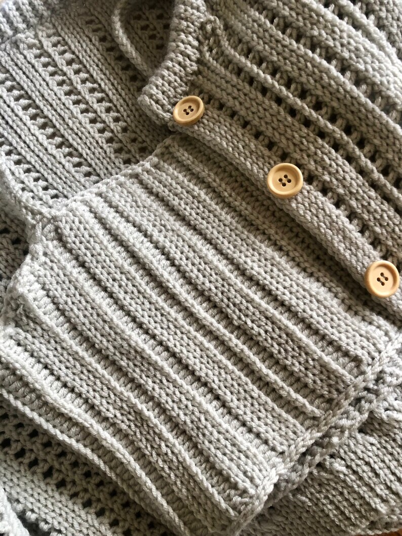 K&ouml;nnte beinhalten: Nahaufnahme eines grauen Strickjackens mit Holzkn&ouml;pfen. Der Cardigan hat ein strukturiertes Strickmuster und ist in der H&auml;lfte gefaltet.