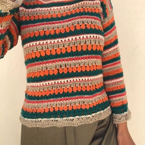 May include: A striped crochet sweater with long sleeves in shades of orange, green, beige, and white. The sweater has a loose fit and a round neckline.