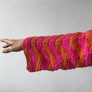 May include: A pink and orange striped crocheted sleeve with a wavy pattern.