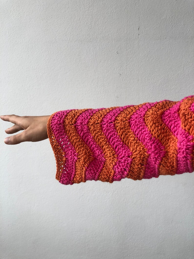 May include: A pink and orange striped crocheted sleeve with a wavy pattern.