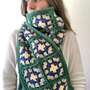 May include: A green, blue, yellow, and beige crocheted scarf with a granny square pattern.
