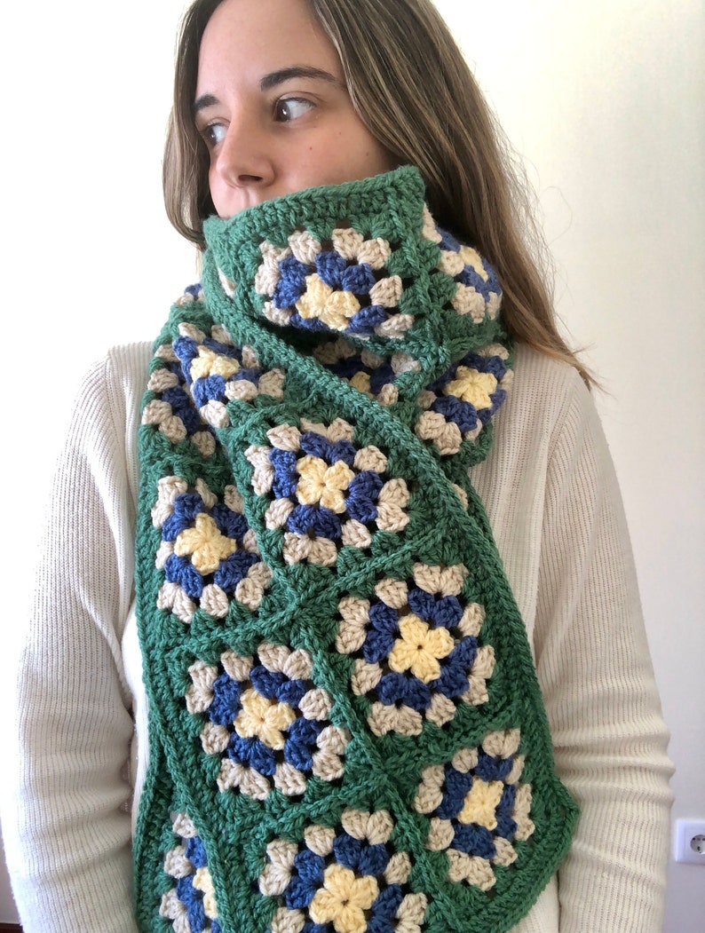 May include: A green, blue, yellow, and beige crocheted scarf with a granny square pattern.
