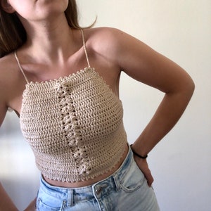 May include: A beige crochet halter top with a delicate crocheted design. The top is cropped and has a relaxed fit.