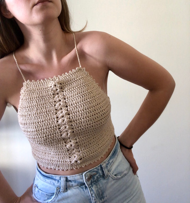 May include: A beige crochet halter top with a delicate crocheted design. The top is cropped and has a relaxed fit.