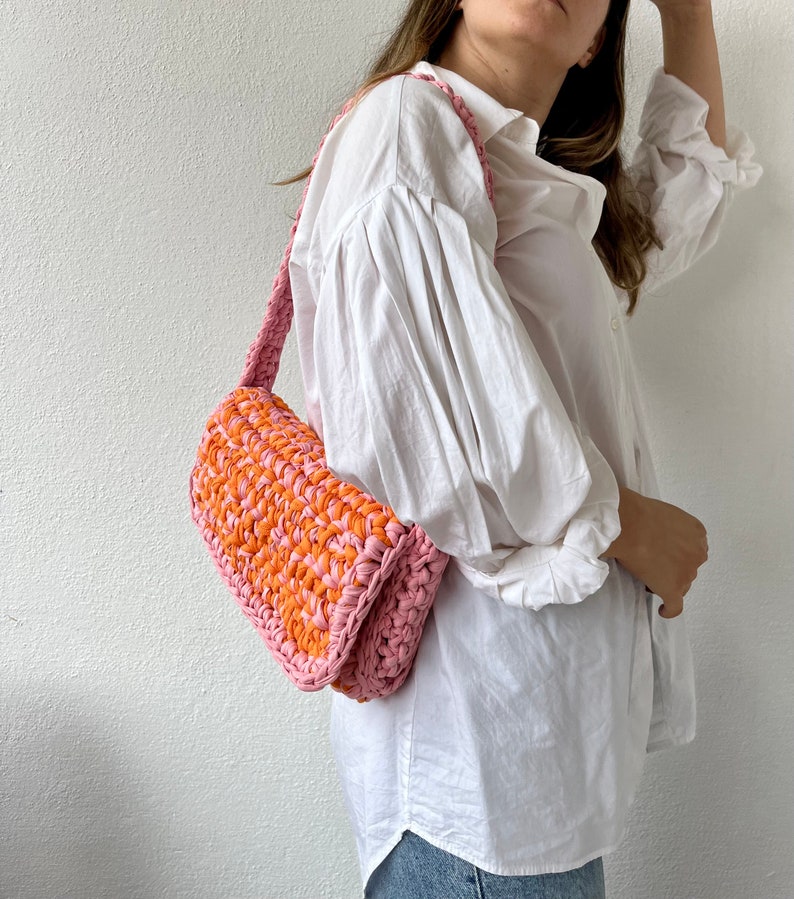 May include: A pink and orange crocheted shoulder bag with a long strap.