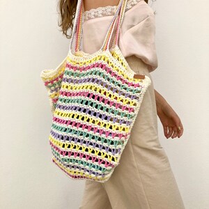 May include: A colorful striped crochet tote bag with a white background. The bag has a wide, open top and two long straps.