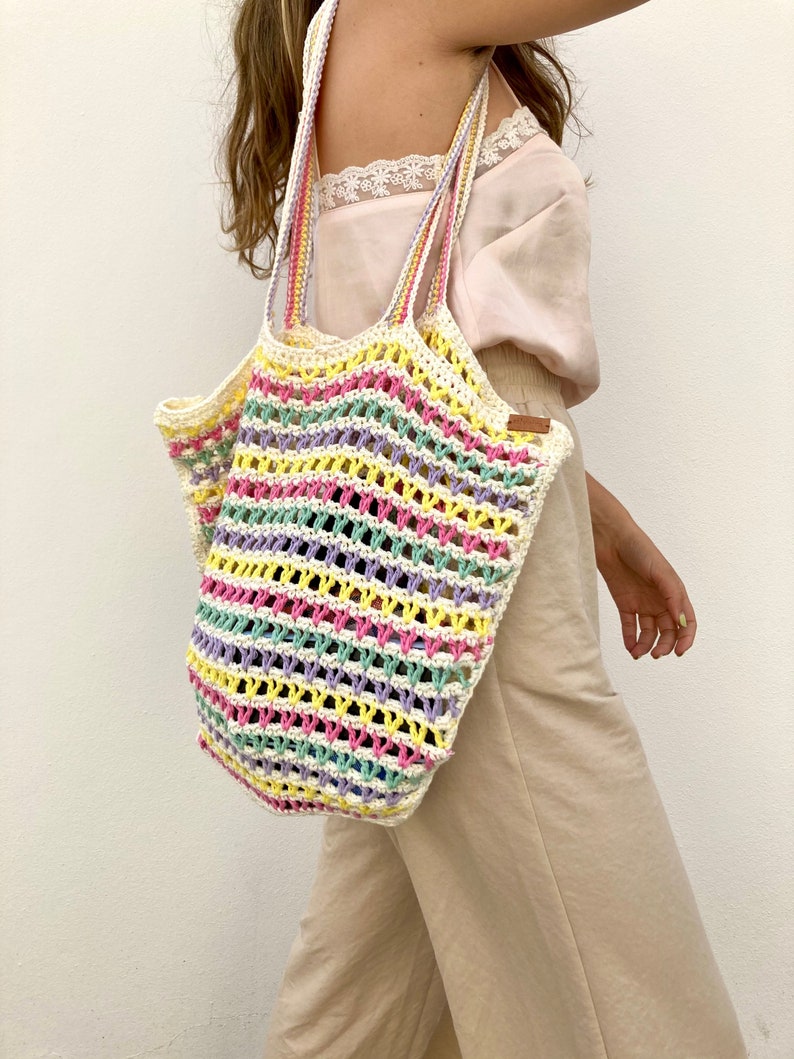 May include: A colorful striped crochet tote bag with a white background. The bag has a wide, open top and two long straps.