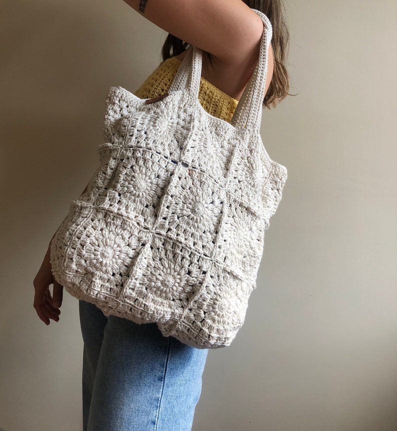 May include: A white crocheted tote bag with a square pattern. The bag has a wide, flat base and two straps.
