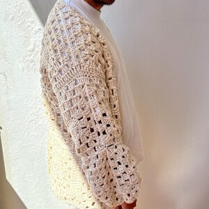 K&ouml;nnte beinhalten: Ein cremefarbener H&auml;kelcardigan mit einem quadratischen Stichmuster. Der Cardigan hat lange &Auml;rmel und eine lockere Passform.