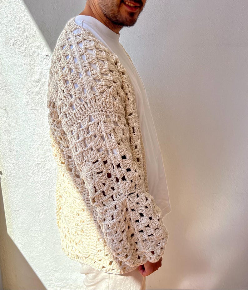 K&ouml;nnte beinhalten: Ein cremefarbener H&auml;kelcardigan mit einem quadratischen Stichmuster. Der Cardigan hat lange &Auml;rmel und eine lockere Passform.