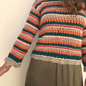 May include: A long-sleeved, striped crochet sweater with a loose fit. The sweater is made with a variety of colors, including green, orange, beige, and white.