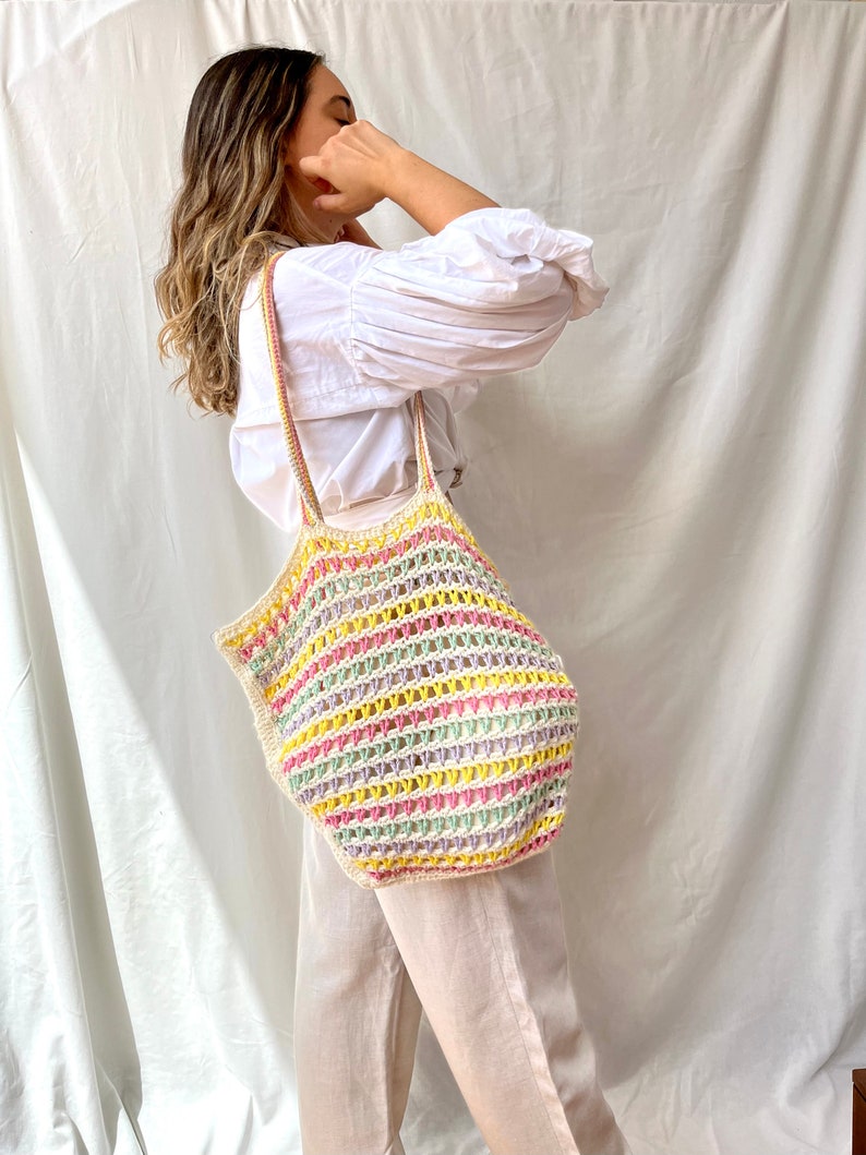 May include: A large, colorful crochet tote bag with a striped pattern in pink, yellow, green, and white. The bag is made of a thick, textured yarn and has a wide, open top.