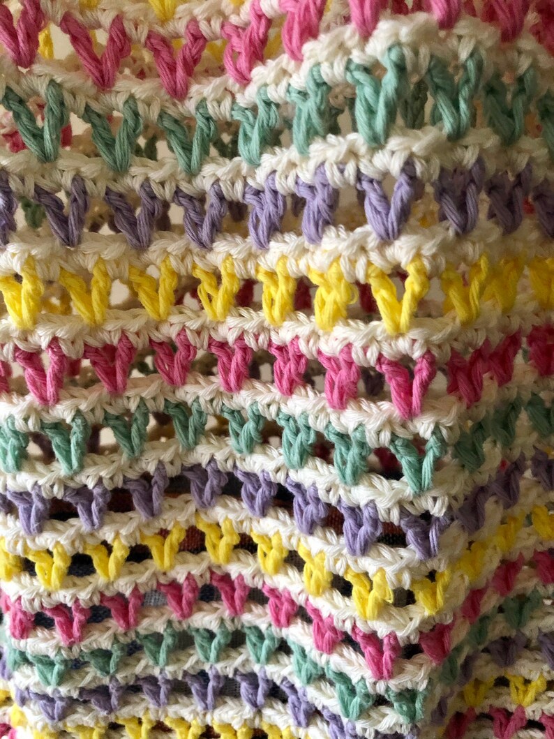 May include: Close-up of a crocheted fabric with a repeating pattern of pink, yellow, green, and purple yarn. The fabric is made with a white yarn base.