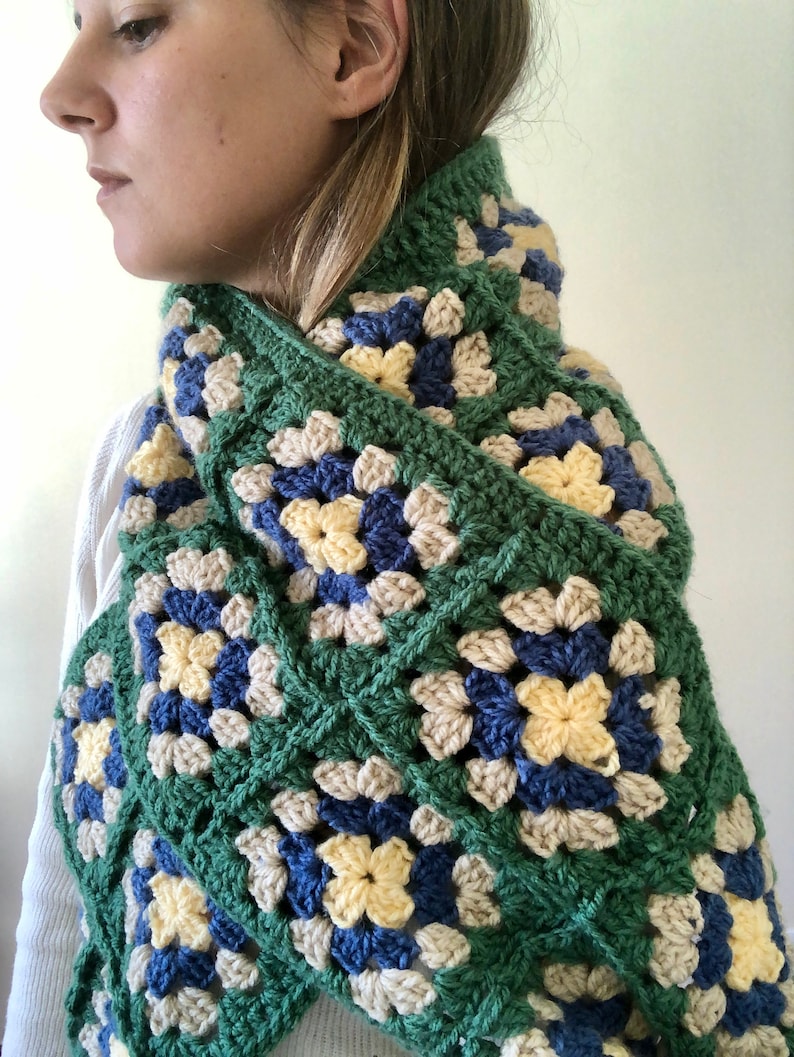 May include: A green, blue, yellow, and beige crocheted scarf with a granny square pattern.