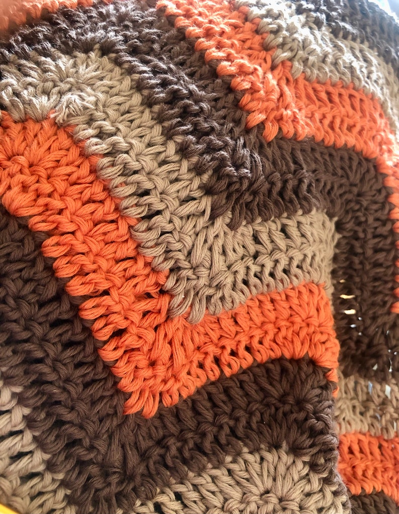 May include: A crocheted blanket with stripes of brown, beige, and orange yarn.