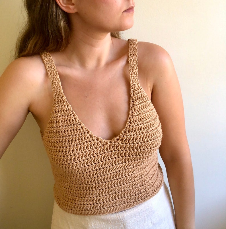 May include: A crocheted tank top in a light brown color. The top has a v-neck and thin straps.