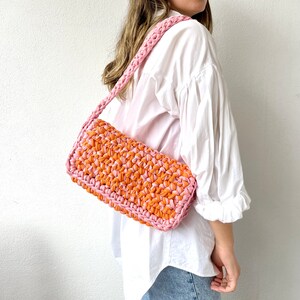 May include: A pink and orange crocheted shoulder bag with a long strap.