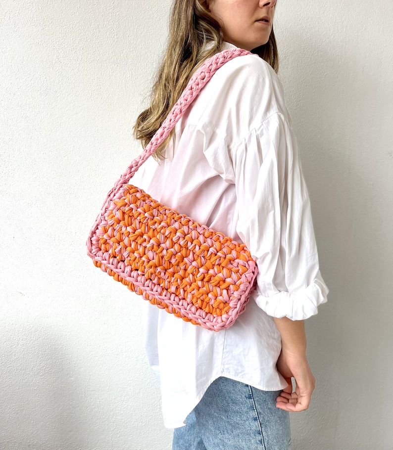 May include: A pink and orange crocheted shoulder bag with a long strap.