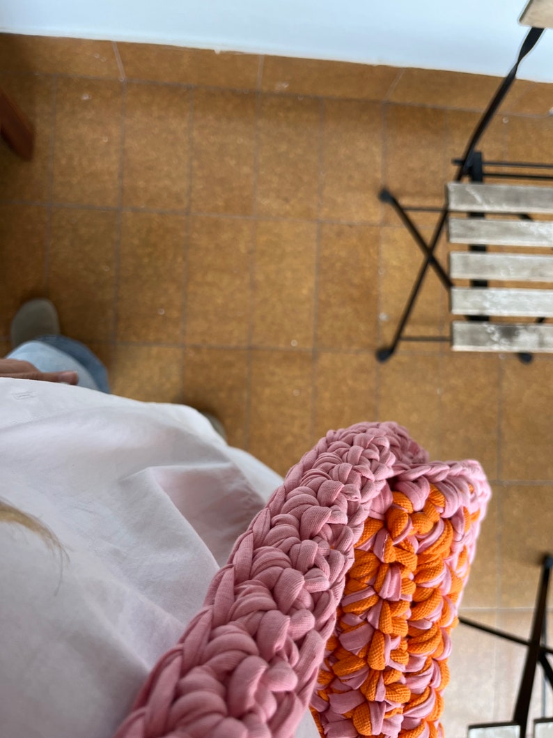 May include: A pink and orange crocheted bag made from fabric strips. The bag is large and has a thick, braided strap.