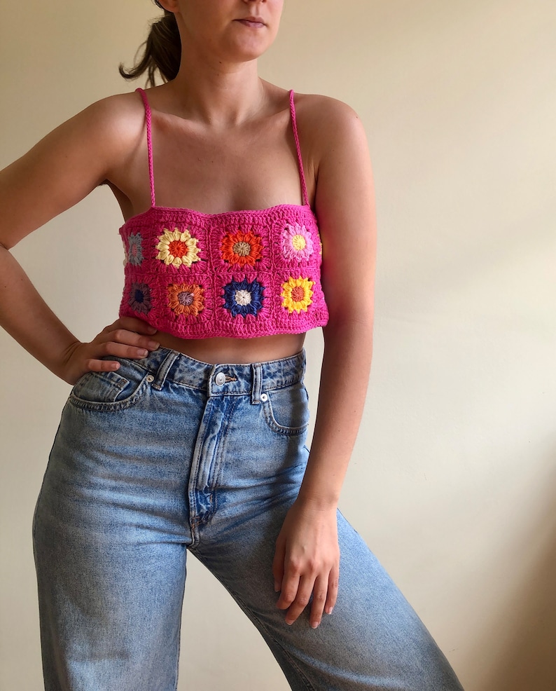 K&ouml;nnte beinhalten: Ein leuchtend pinkes H&auml;keltop mit floralem Design. Das Top hat ein quadratisches Muster mit bunten Blumenmotiven in Gelb, Orange, Blau und Rosa. Es wird mit hellblauen Jeans kombiniert.
