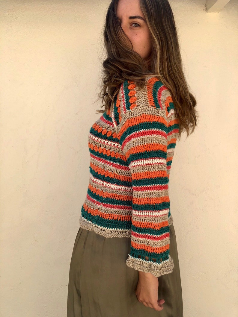 May include: A striped crochet top with a colorful pattern in shades of orange, green, beige, and red. The top has a crocheted trim around the neckline and sleeves.