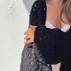 May include: A black crochet cardigan with a loose fit and open front. The cardigan has a delicate, lacy pattern and is made with a soft, textured yarn.