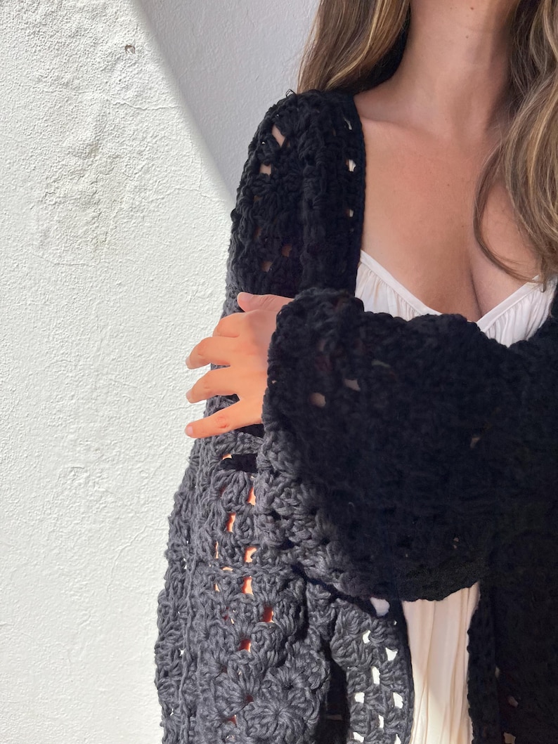 May include: A black crochet cardigan with a loose fit and open front. The cardigan has a delicate, lacy pattern and is made with a soft, textured yarn.