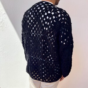 K&ouml;nnte beinhalten: Ein schwarzer H&auml;kelcardigan mit einem gro&szlig;en, offenen Stichmuster. Der Cardigan ist lang&auml;rmelig und hat eine lockere Passform.