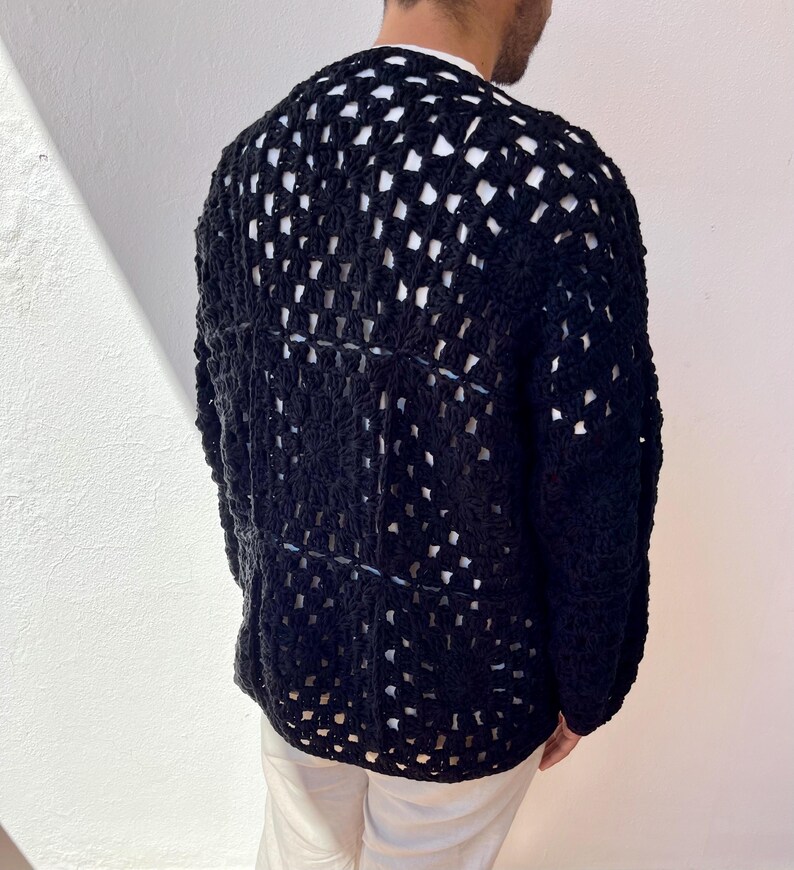 K&ouml;nnte beinhalten: Ein schwarzer H&auml;kelcardigan mit einem gro&szlig;en, offenen Stichmuster. Der Cardigan ist lang&auml;rmelig und hat eine lockere Passform.