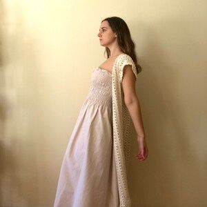 Puede incluir: Una mujer con un c&aacute;rdigan de crochet blanco sobre un vestido blanco con pliegues.