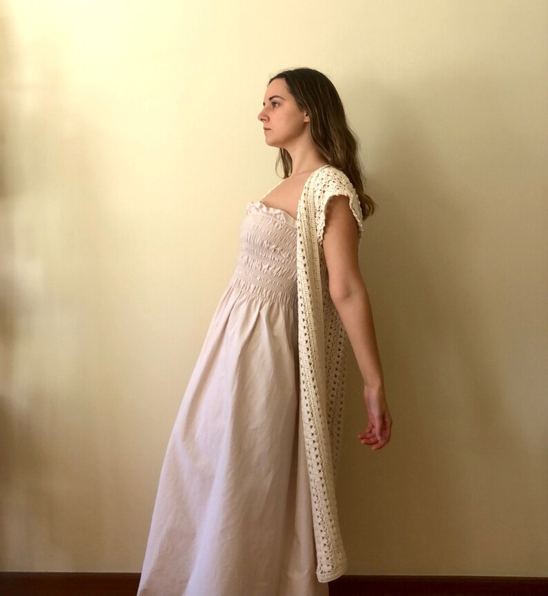 Puede incluir: Una mujer con un c&aacute;rdigan de crochet blanco sobre un vestido blanco con pliegues.