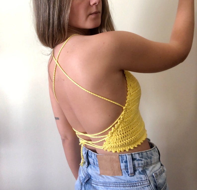 May include: A yellow crochet top with a criss-cross back design. The top is tied at the back and has a scalloped hem.